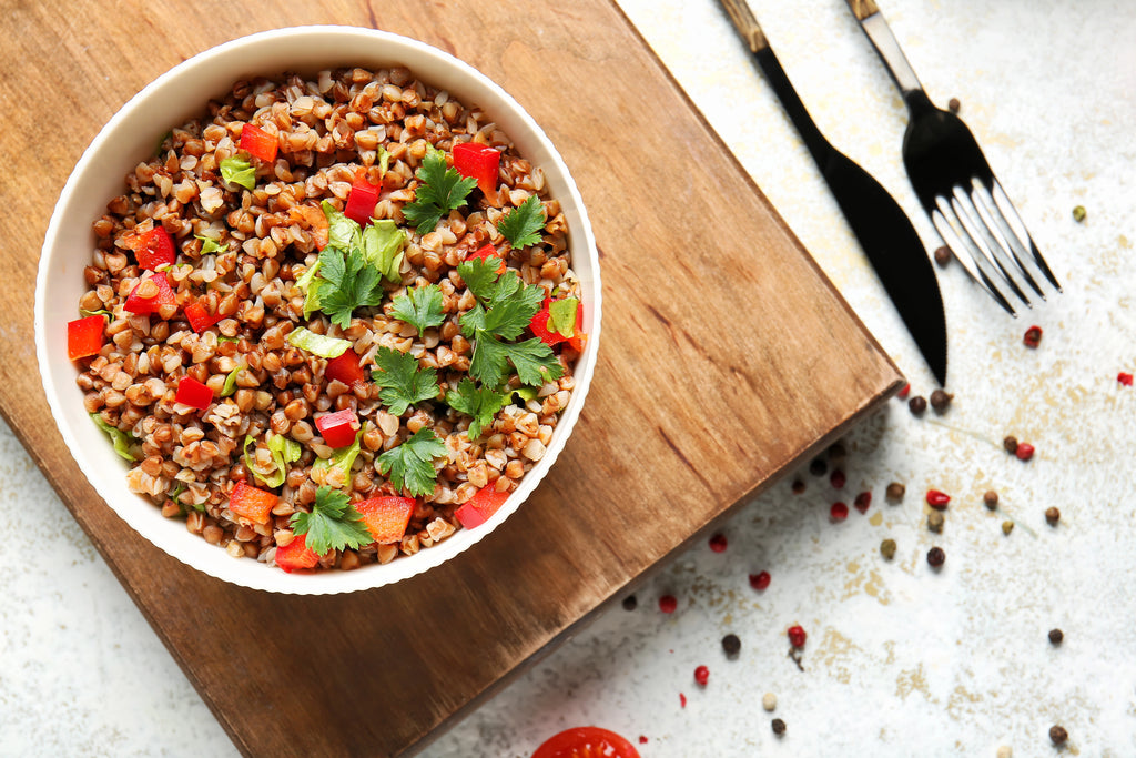 Bowl of buckwheat salad with vegetables on a wooden cutting board