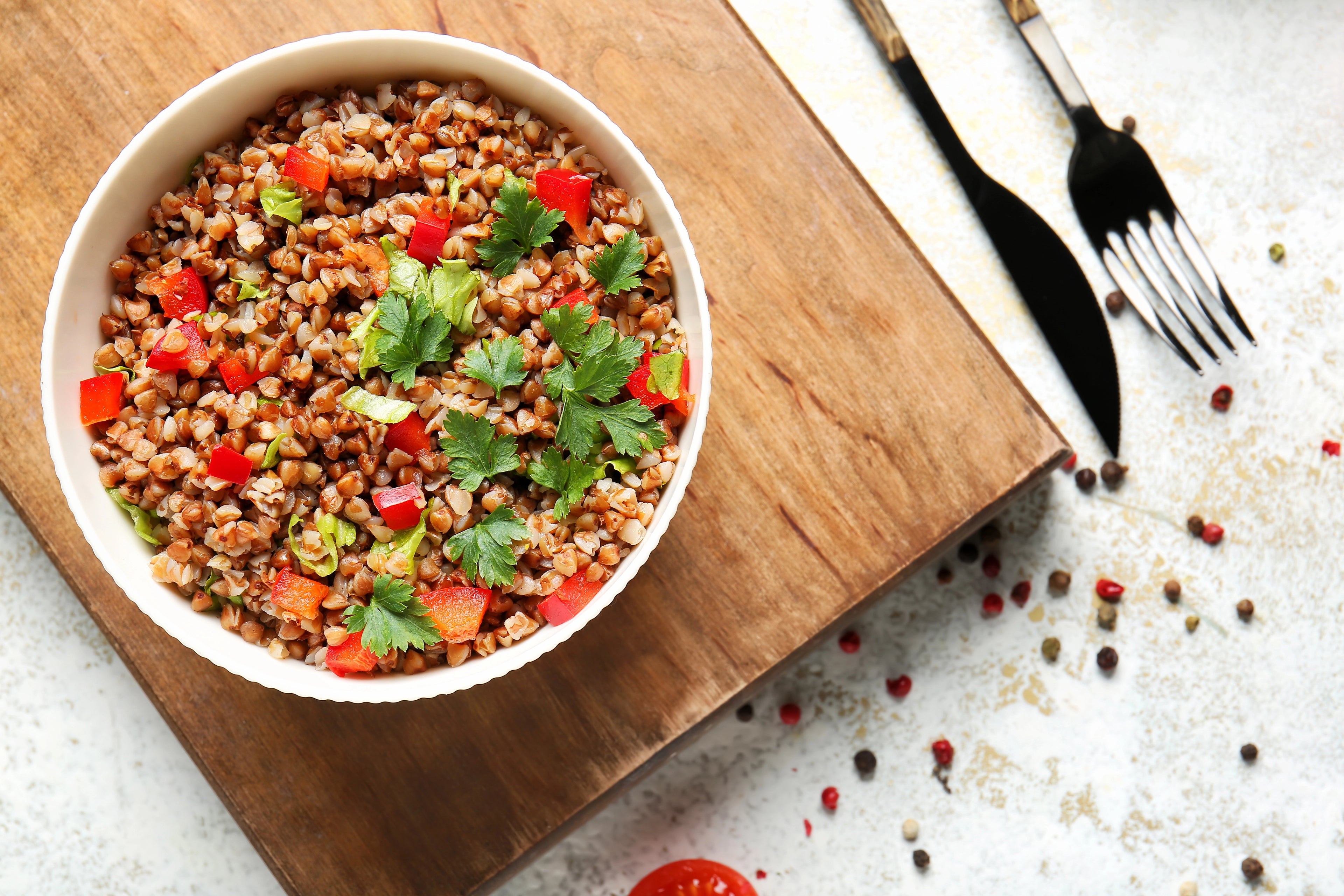 Bowl of buckwheat salad with vegetables on a wooden cutting board